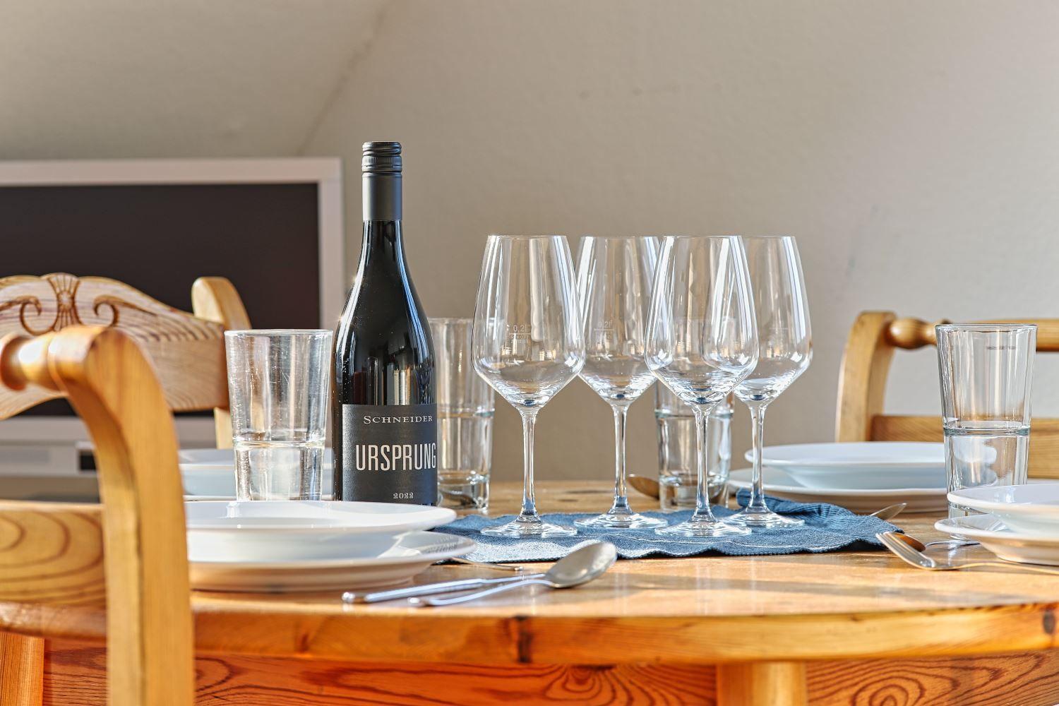 Gedeckter Holztisch mit Weinglas, Wasser und Weinflasche.