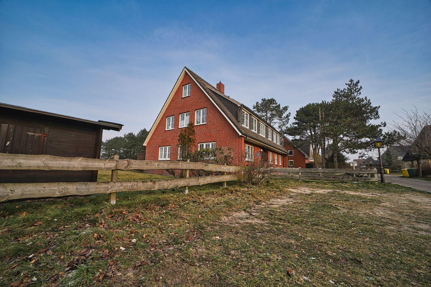 Rotes Backsteinhaus mit Holzzaun und Bäumen im Hintergrund.