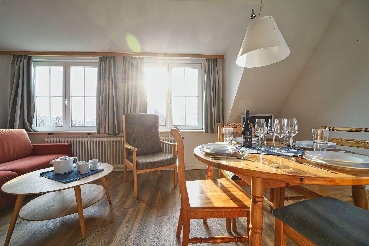 Ein Raum mit Esstisch, Sofa und Fenstern. Sonne fällt durch die Fenster.