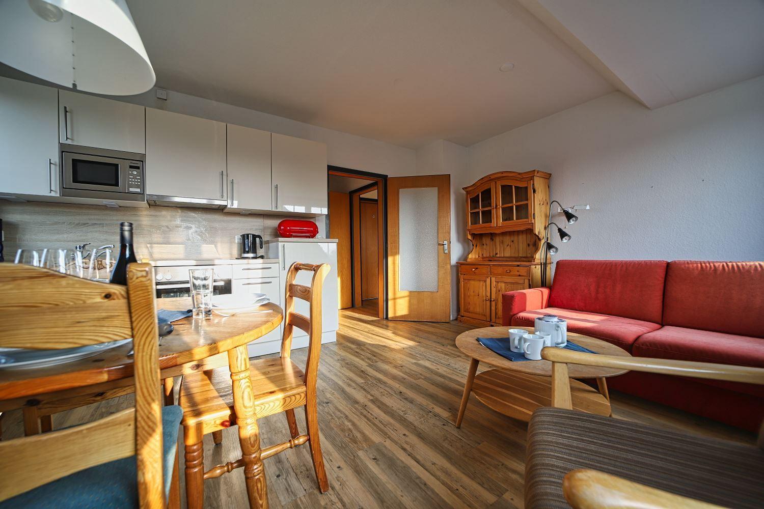 Wohnküche mit Essbereich, rotem Sofa und Holzmöbeln.