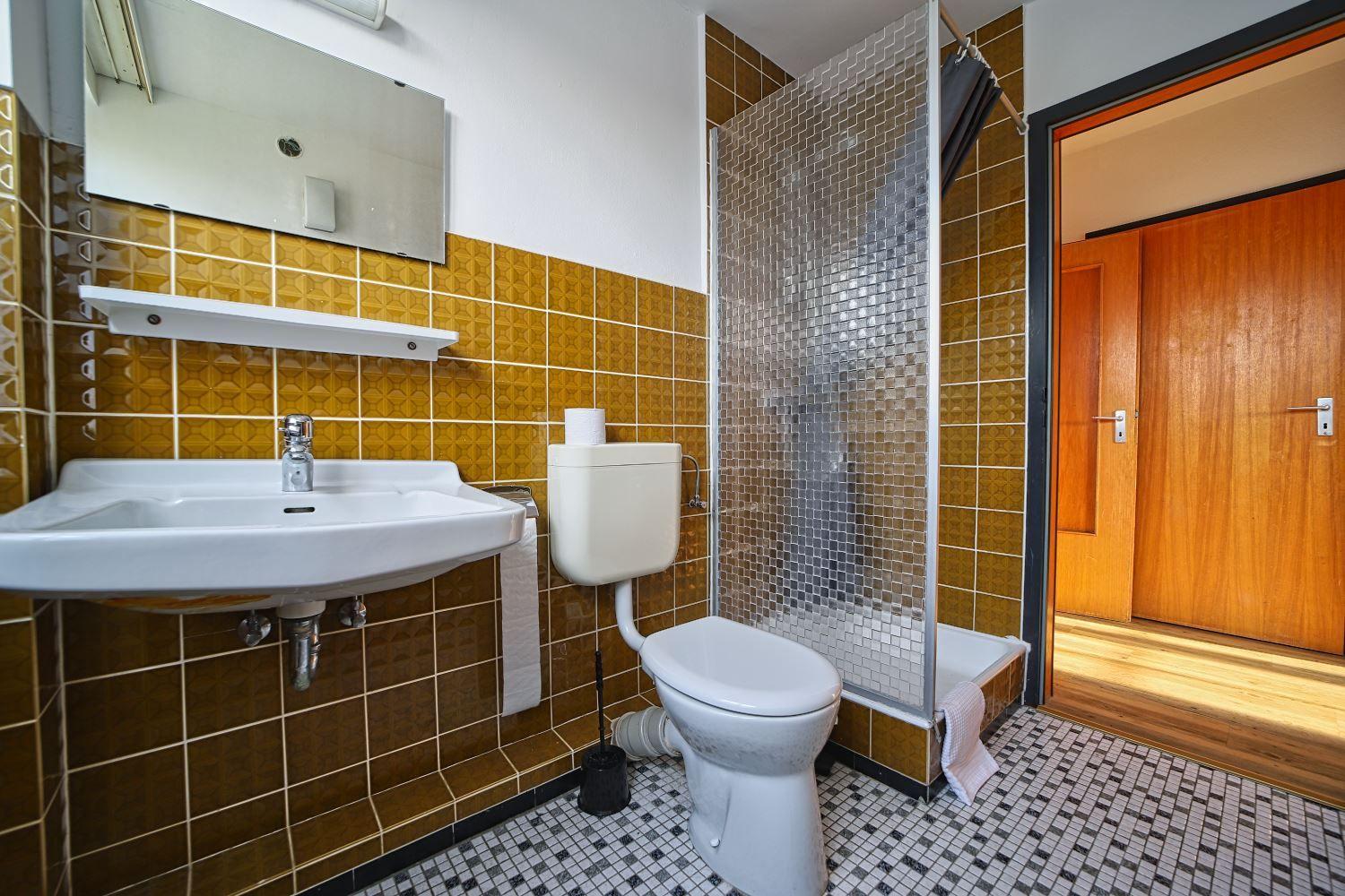 Badezimmer mit Dusche, Waschbecken und Toilette. Wandfliesen und Mosaikboden.