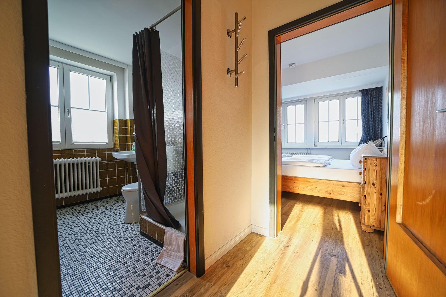 Badezimmer mit Dusche und Toilette. Nebenraum mit Bett und Holzboden.