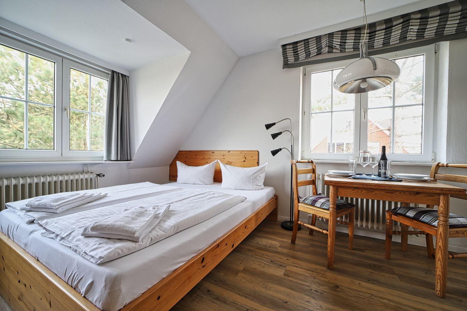 Schlafzimmer mit Bett, Tisch und Stühlen. Fenster mit Blick auf Bäume.