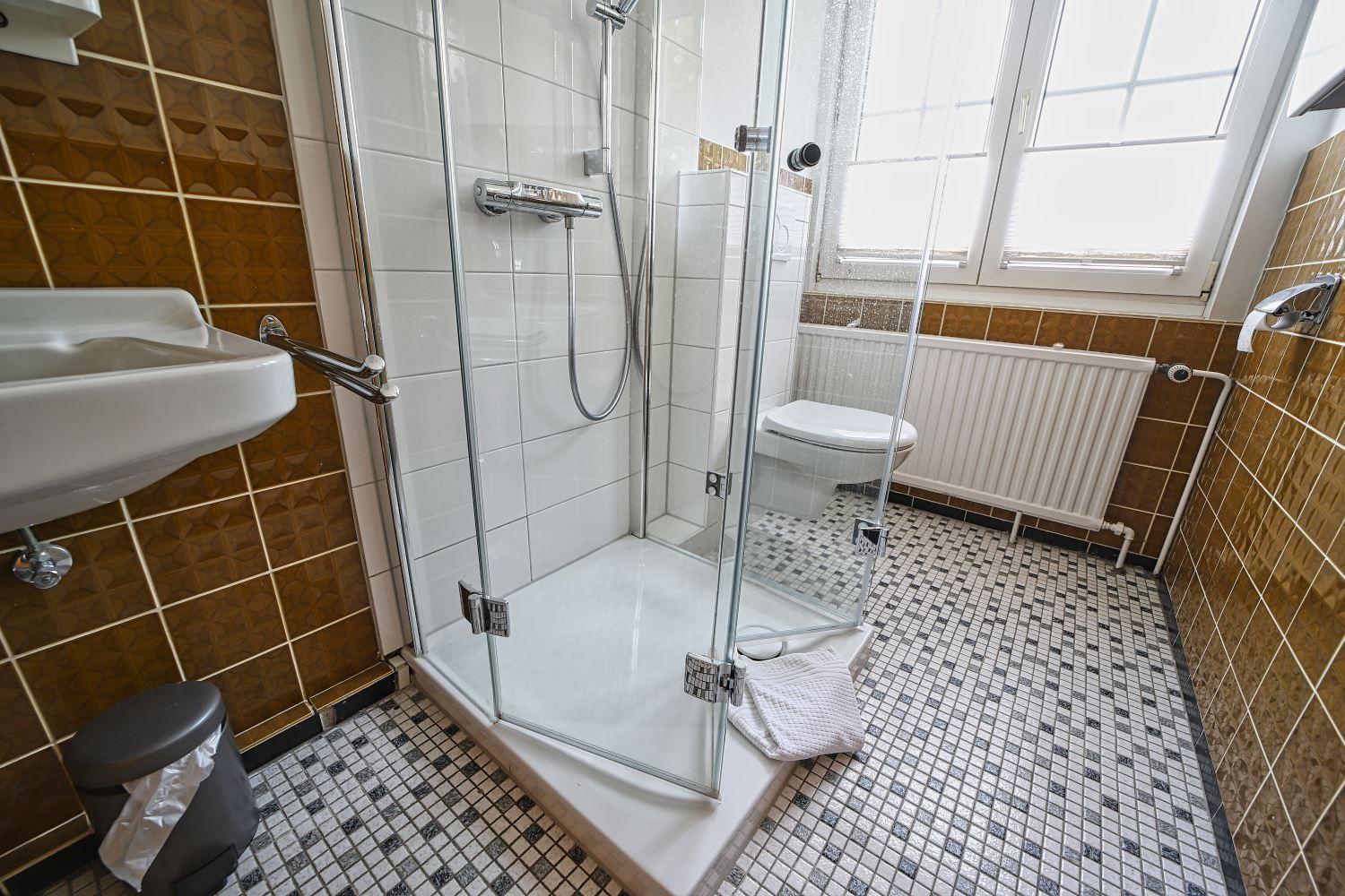 Bad mit Dusche, Toilette und Waschbecken. Fliesenboden und Fenster.