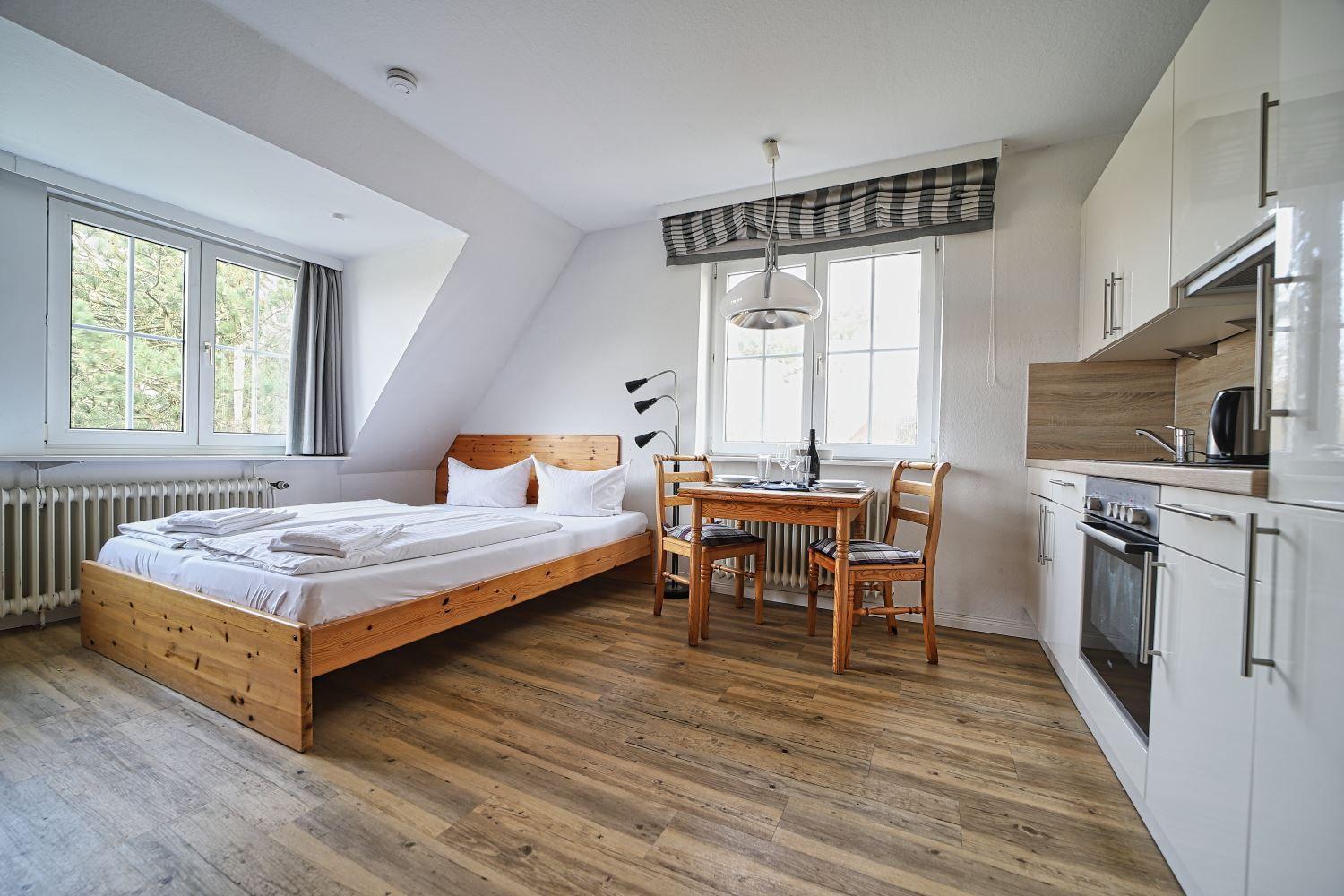 Schlafzimmer mit Bett, Essplatz und Küche. Holzboden und große Fenster.