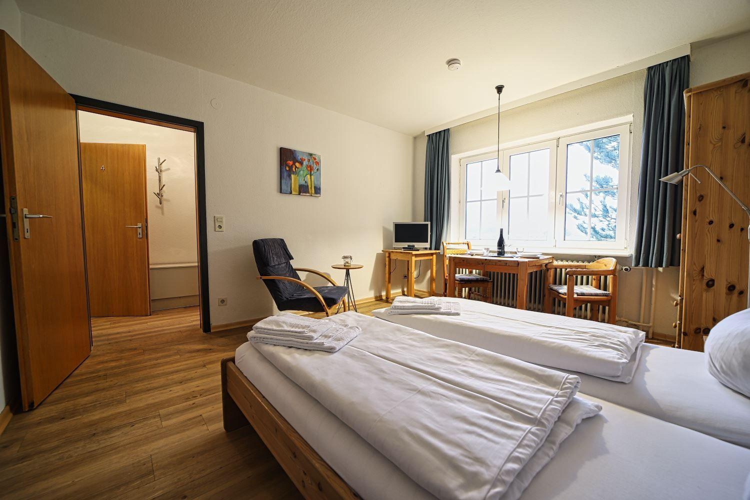 Zwei Betten, Tisch mit Stühlen, Fenster mit Blick, Holzboden und Tür zum Bad.