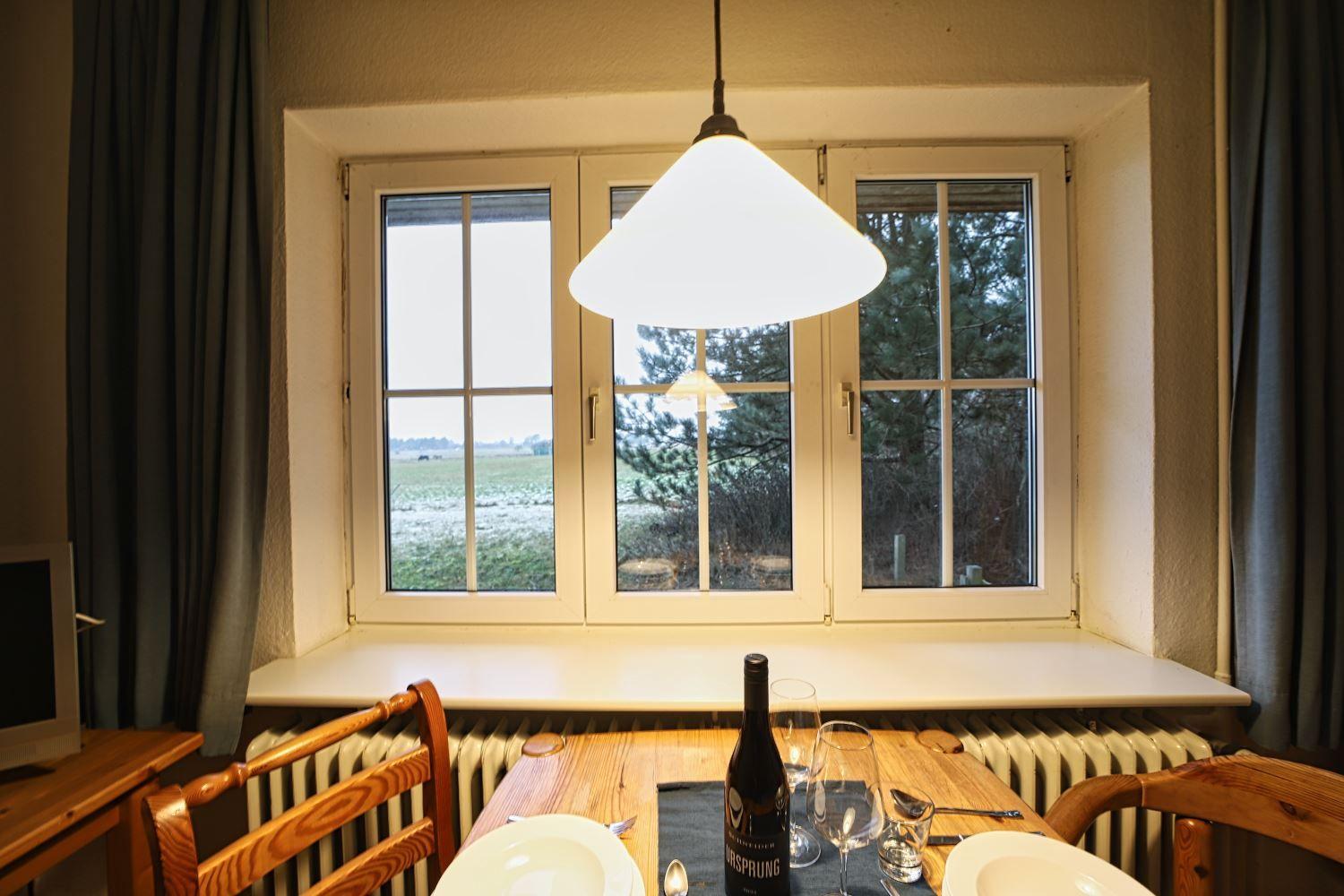 Esszimmer mit Tisch, Stühlen und Fensterblick auf Feld und Bäume.