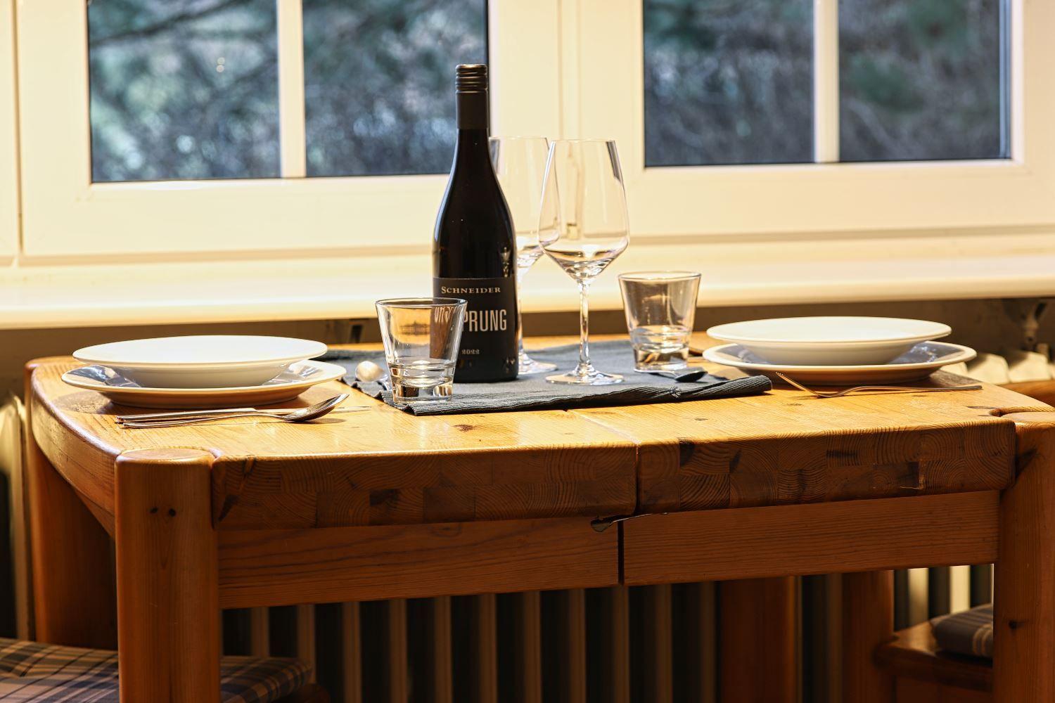 Holztisch mit zwei Platzsetzungen, Weinkrug und Fensterblick.