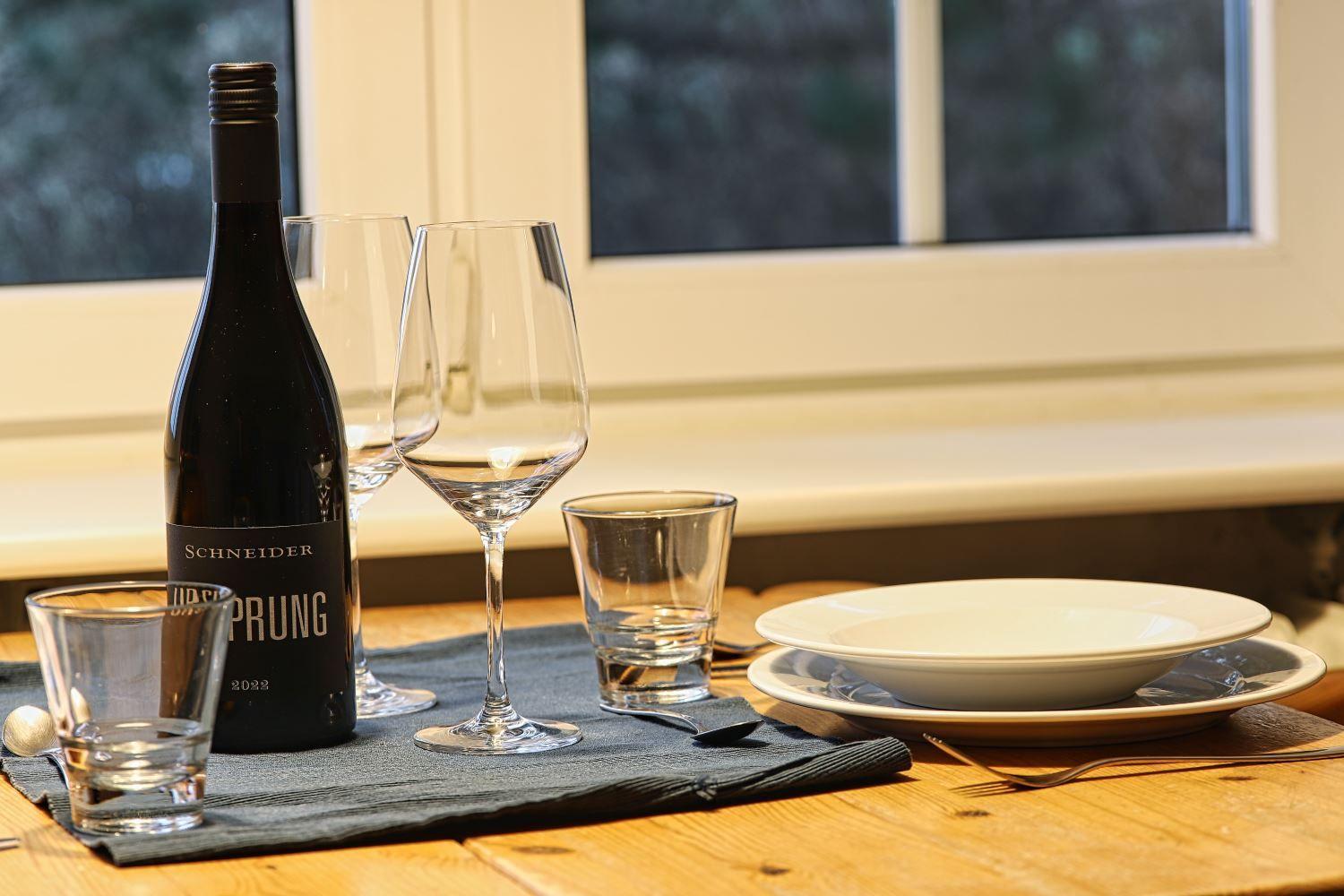 Tisch mit Weinflasche, Gläsern und Geschirr vor Fenster