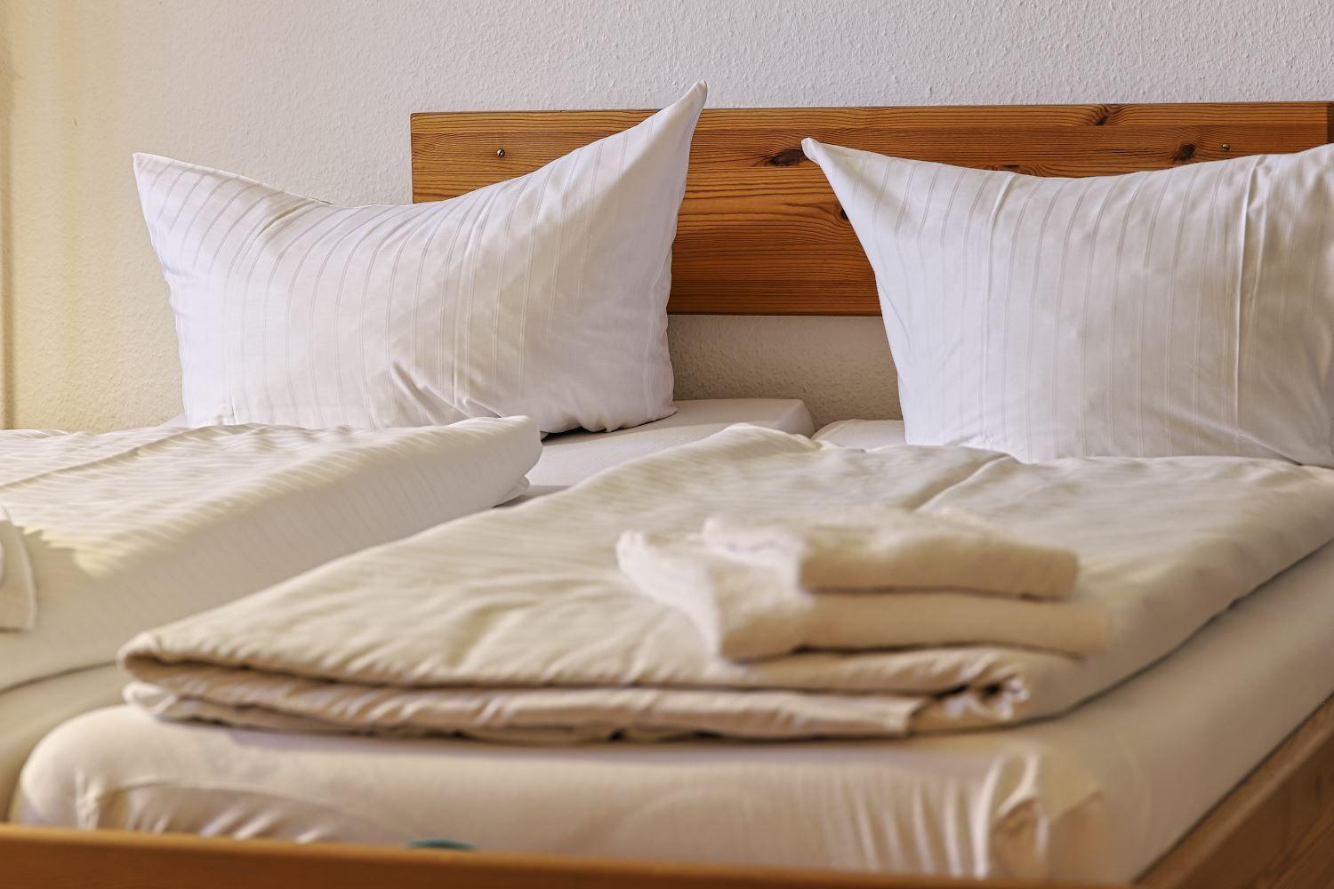 Zwei Betten mit weißen Kissen und Bettwäsche. Holzgestell und gefaltete Decke.