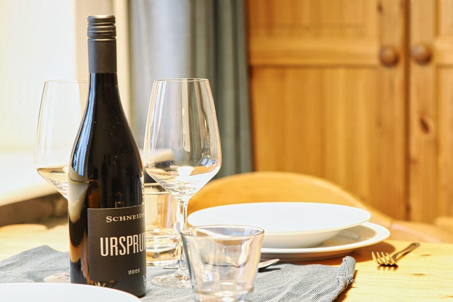 Tisch gedeckt mit Weinglas, Flasche und Geschirr. Holzmöbel und Tischtuch.