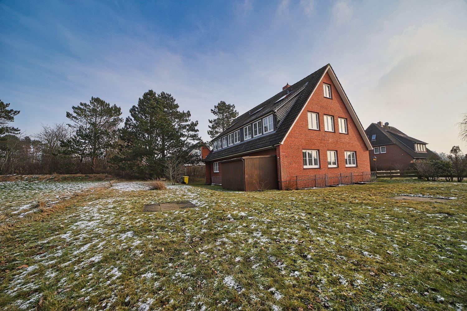 Rotes Backsteinhaus mit Schneebedecktem Rasen und Bäumen im Hintergrund.