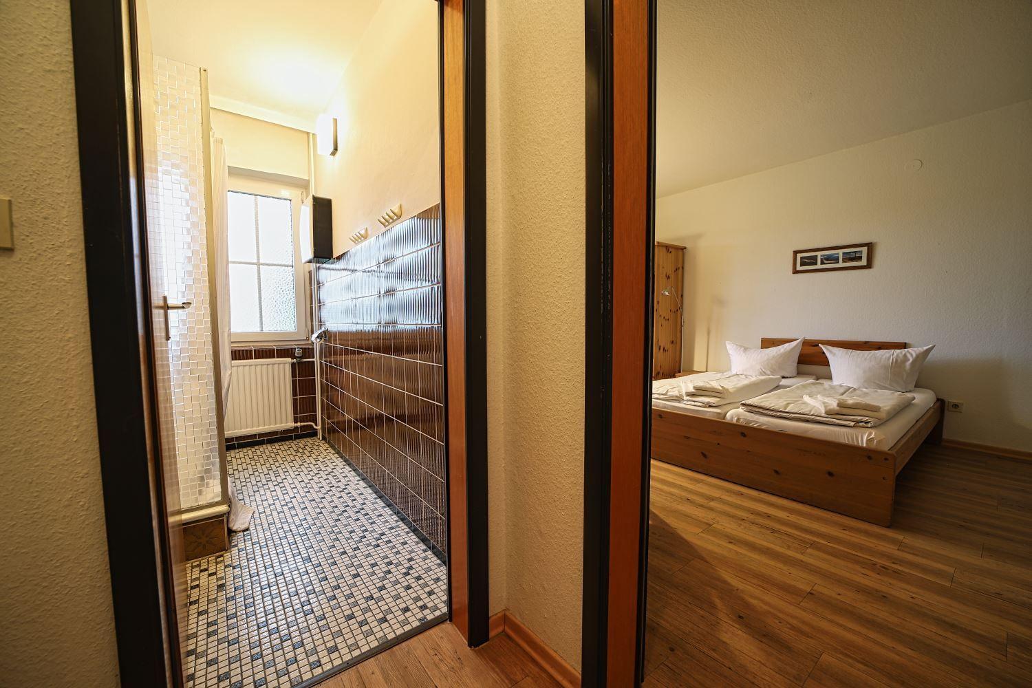 Schlafzimmer mit Holzbett und Badezimmer mit Mosaikfliesen