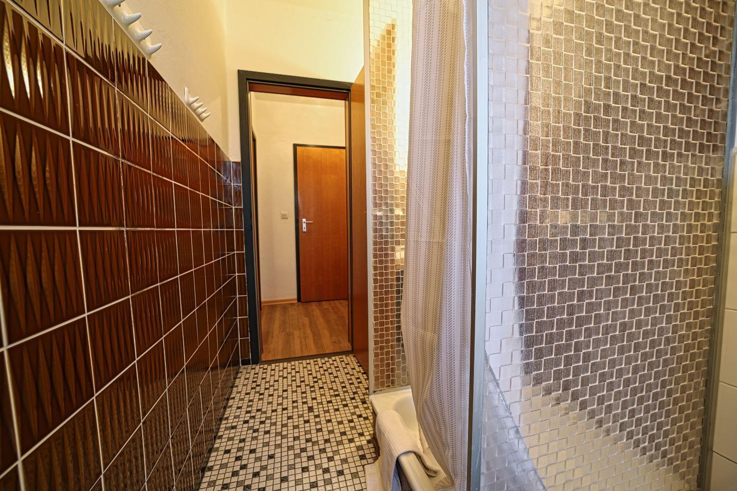 Badezimmer mit Dusche, Mosaikfliesen und Holzboden im Flur.