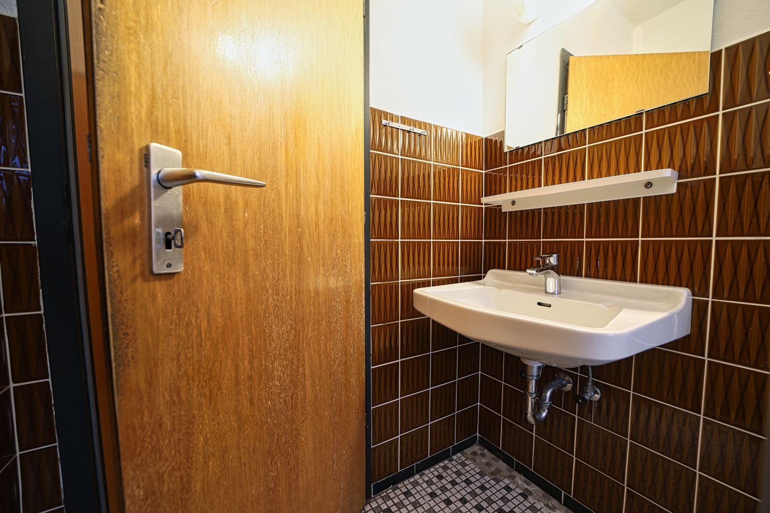 Badezimmer mit Waschbecken, Spiegel und Holztür.