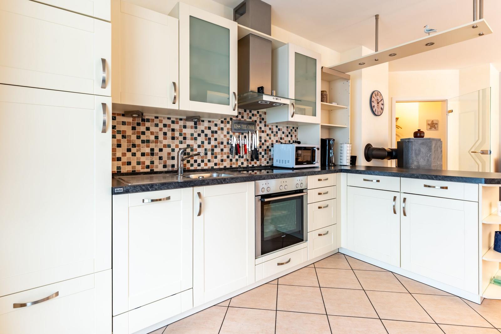 Küche mit weißen Schränken, Mosaikwand und Edelstahlgeräten.