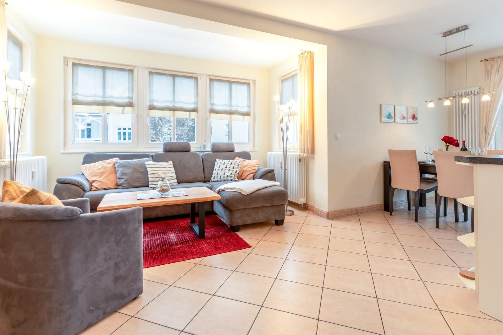 Wohn- und Essbereich mit Sofa, Tisch und Fenstern.