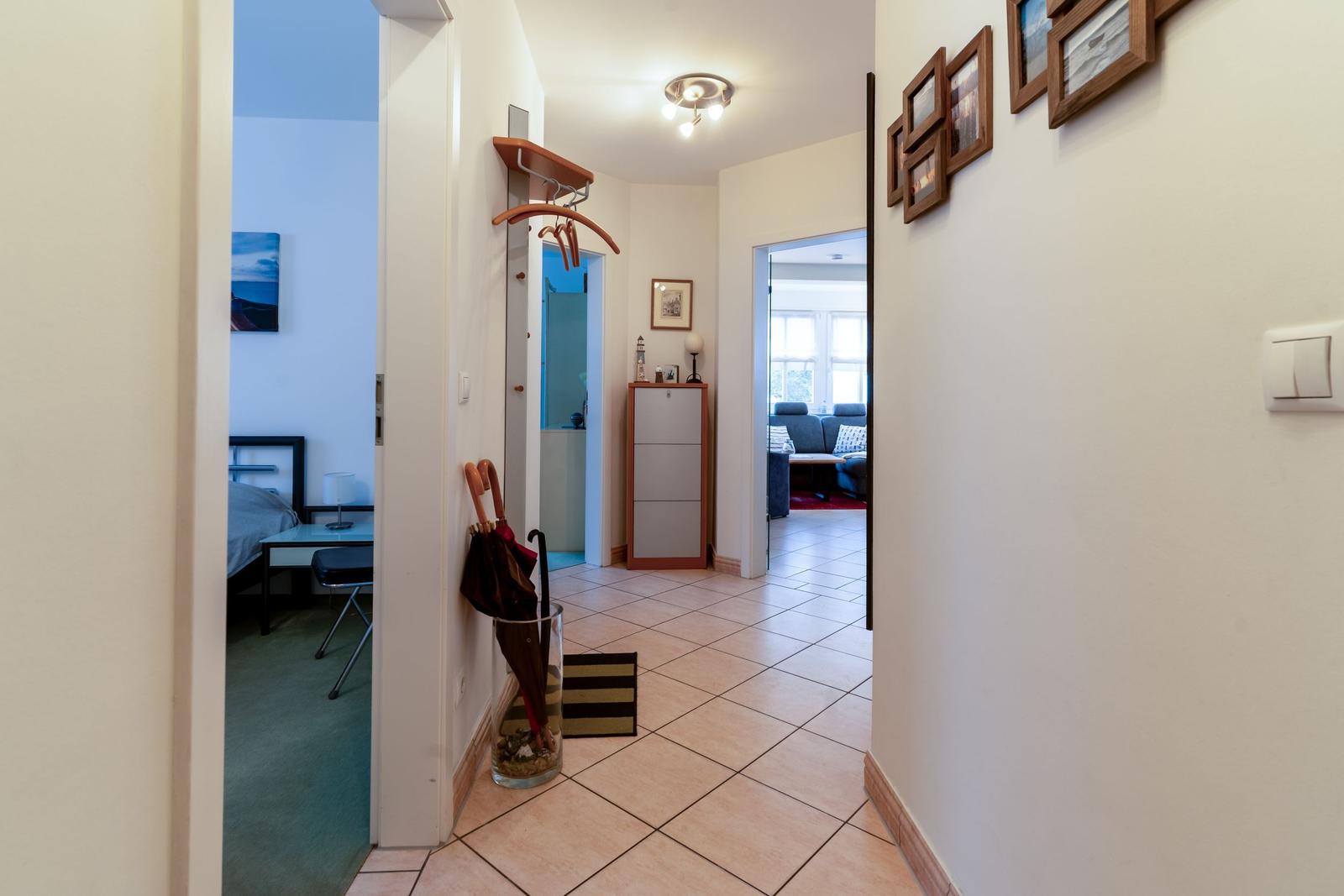 Flur mit Blick in Schlafzimmer und Wohnzimmer. Regal, Regenschirm und Bilder an der Wand.