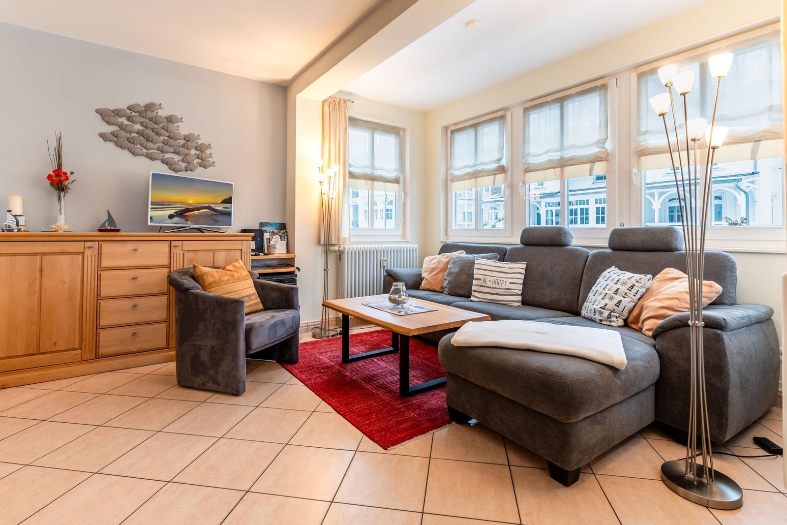 Wohnzimmer mit grauem Sofa, rotem Teppich und Holzmöbeln.