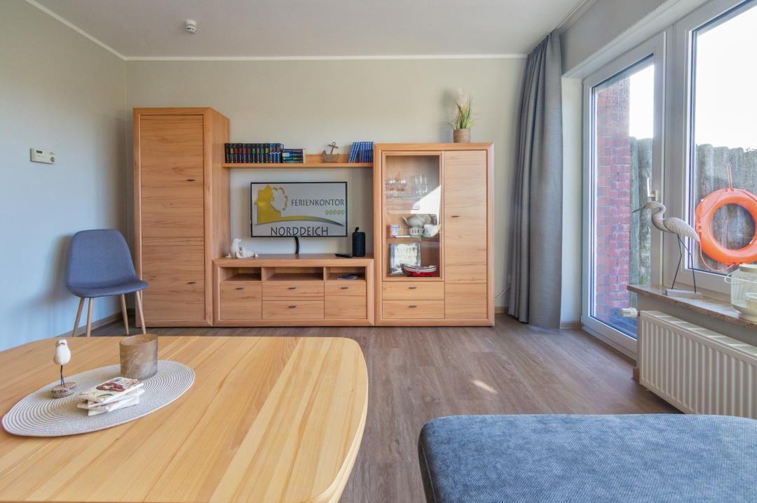 Wohnzimmer mit Holzmöbeln, TV und großem Fenster mit Blick auf Außenbereich.