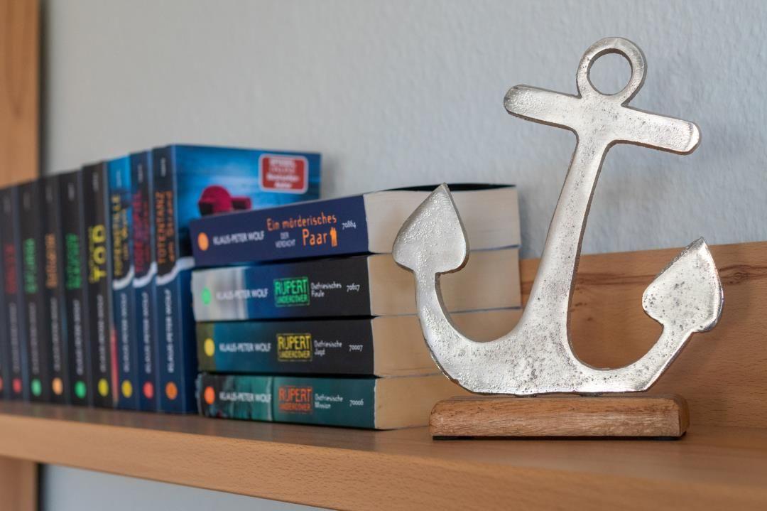 Ein silbernes Ankerobjekt steht auf einem Holzregal neben Büchern.