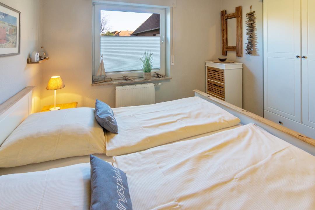 Schlafzimmer mit Doppelbett, Fenster, Schrank und Nachttisch.