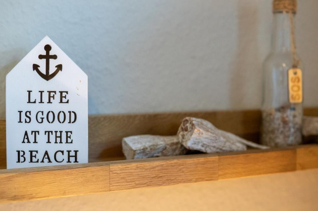 Ein Schild mit Anker und Text steht auf einem Holzregal neben Steinen und einer Flasche.