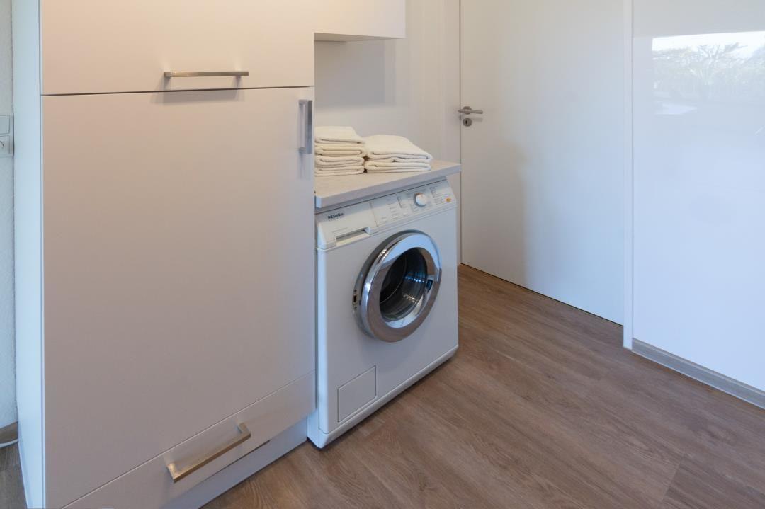Wäschetrockner und Waschmaschine in einem Raum mit Holzfußboden und weißen Schränken.