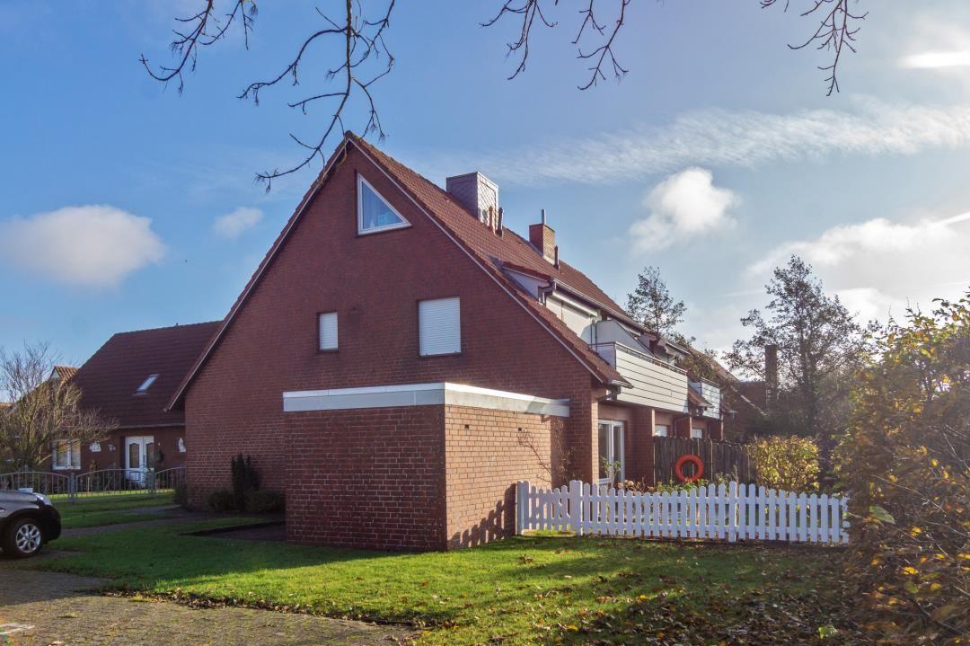 Rotes Backsteinhaus mit weißem Zaun und grünem Rasen.