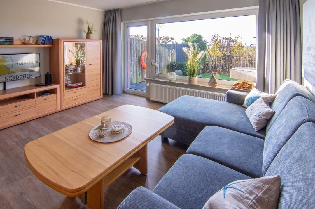 Wohnzimmer mit blauem Sofa, Holztisch und Blick auf Garten
