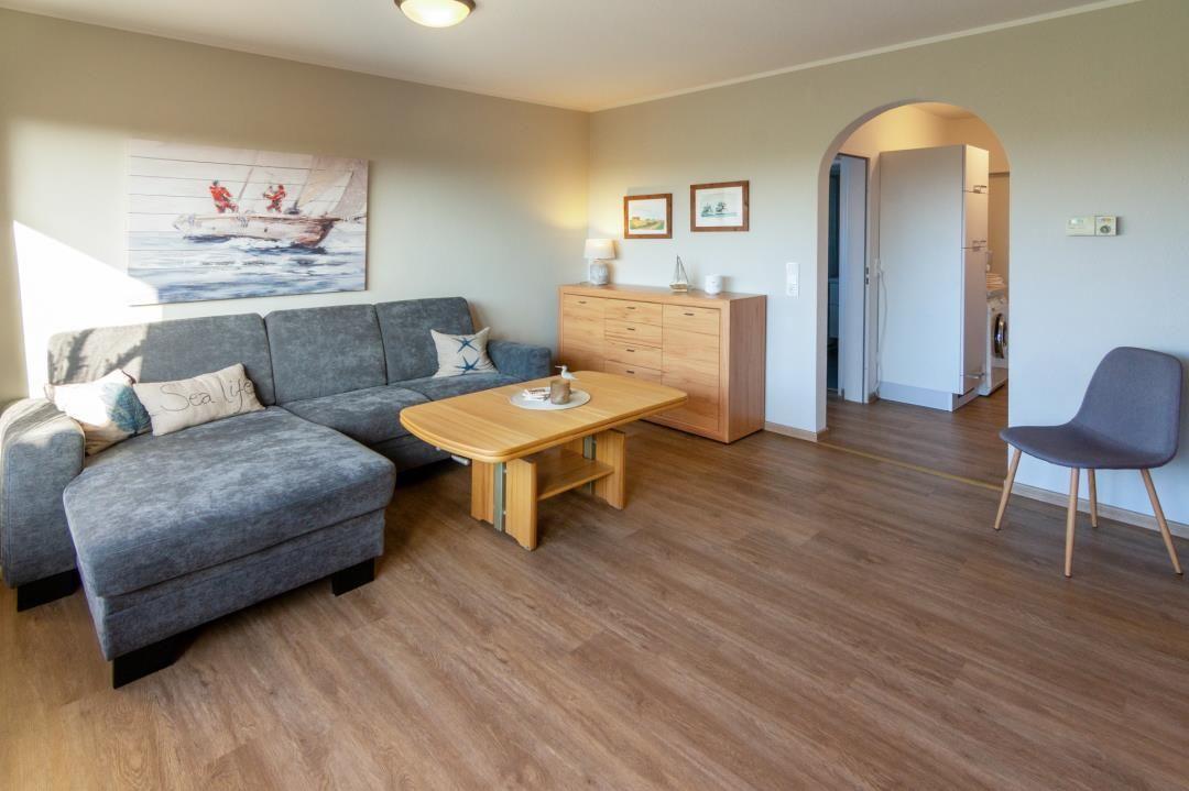 Wohnzimmer mit Sofa, Tisch und Holzboden. Durchgang zur Küche sichtbar.