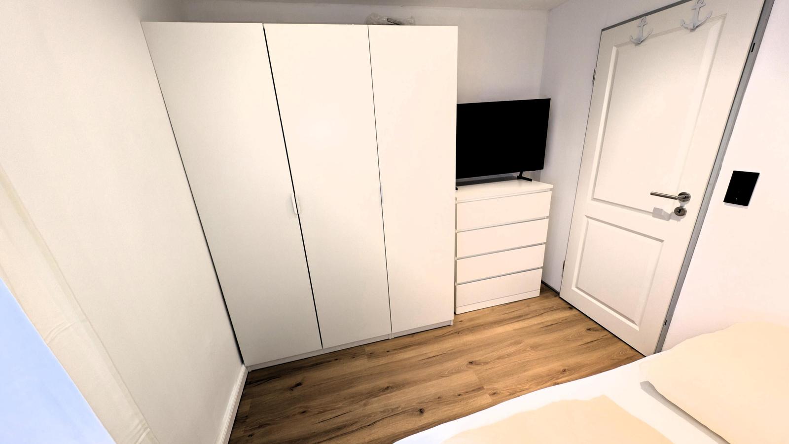Schlafzimmer mit weißen Schränken, TV und Holzboden