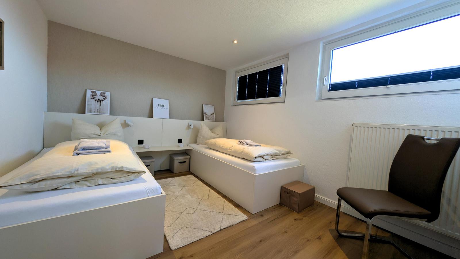 Zimmer mit zwei Betten, Schreibtisch, Stuhl und Fenstern.