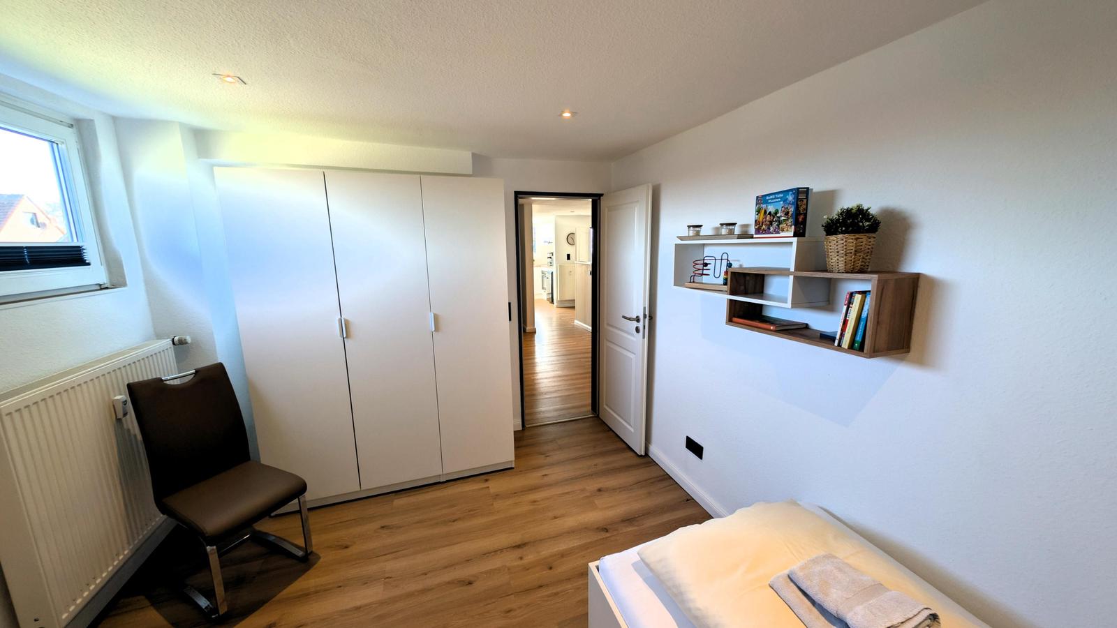 Schlafzimmer mit Bett, Kleiderschrank und Fenster. Anschluss zur Küche.