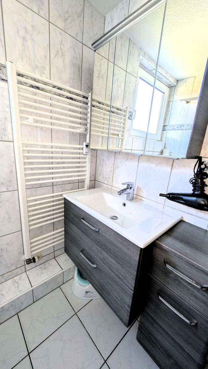 Bad mit Waschbecken, Spiegel und Heizkörper an der Wand.