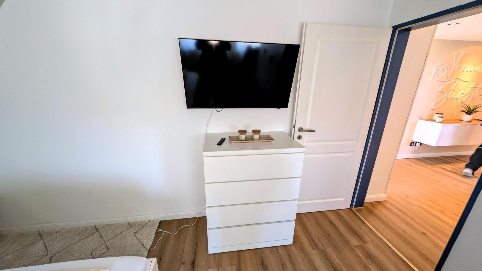 Schlafzimmer mit Fernseher, Schrank und Tür zum Flur.
