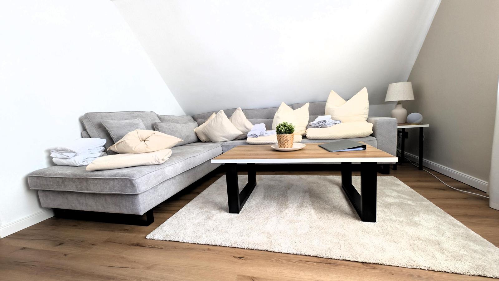 Ein Wohnzimmer mit grauem Sofa, Holztisch und Teppich auf Holzboden.