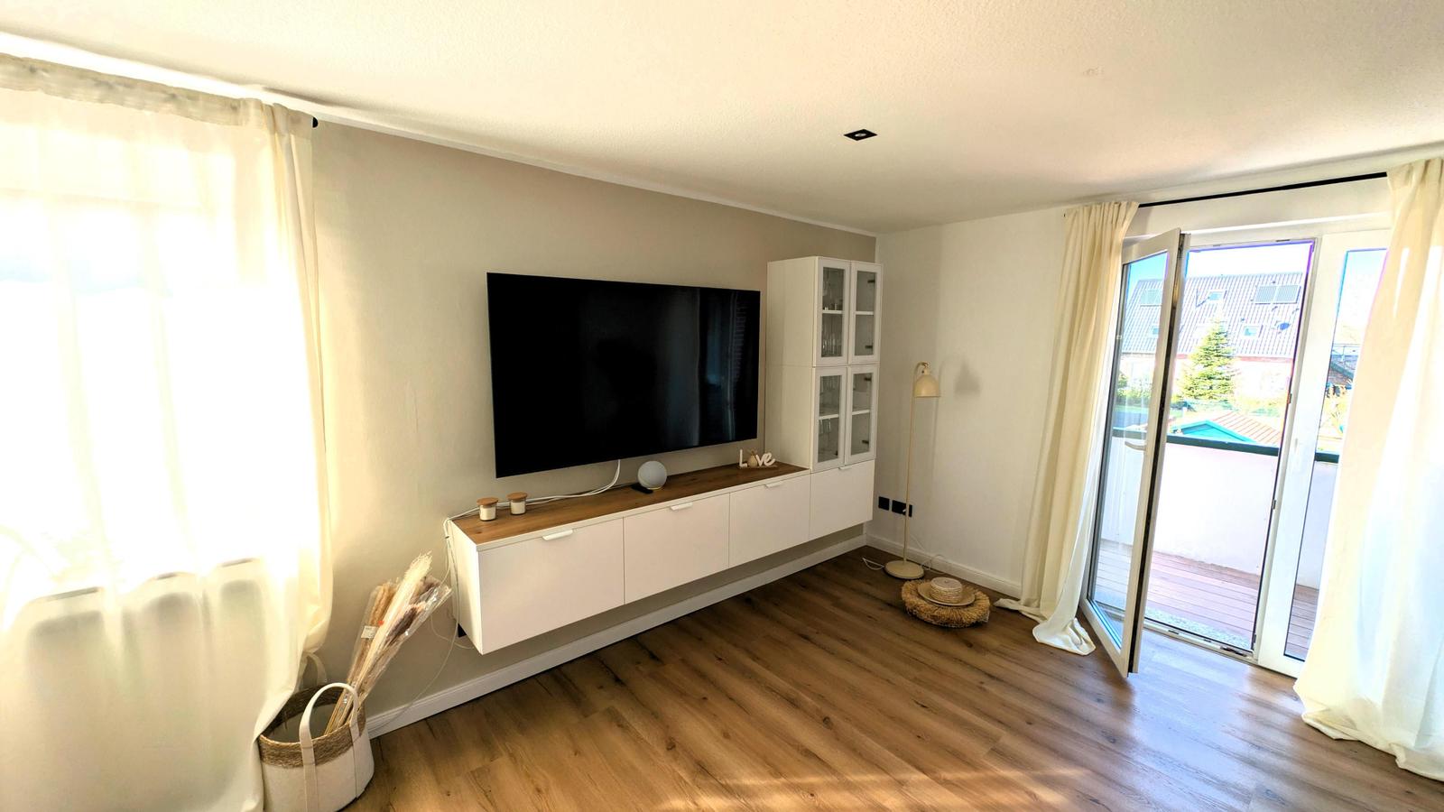 Wohnzimmer mit Fernseher, Holzboden und Terrassentür.