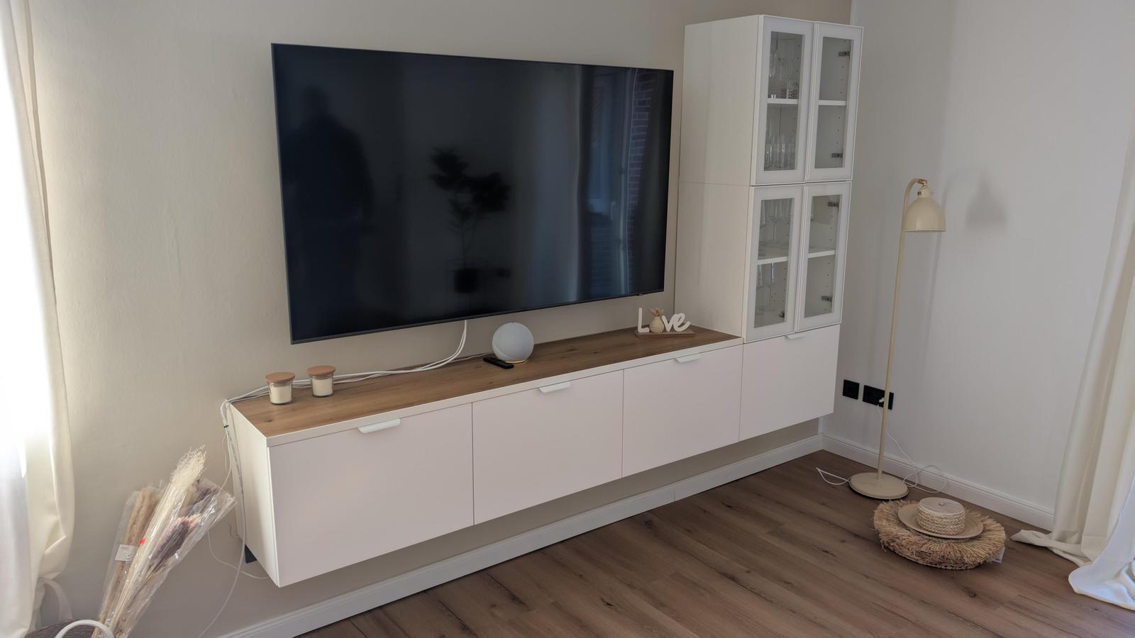 Wohnzimmer mit Fernseher, Schrank und Stehlampe auf Holzboden.