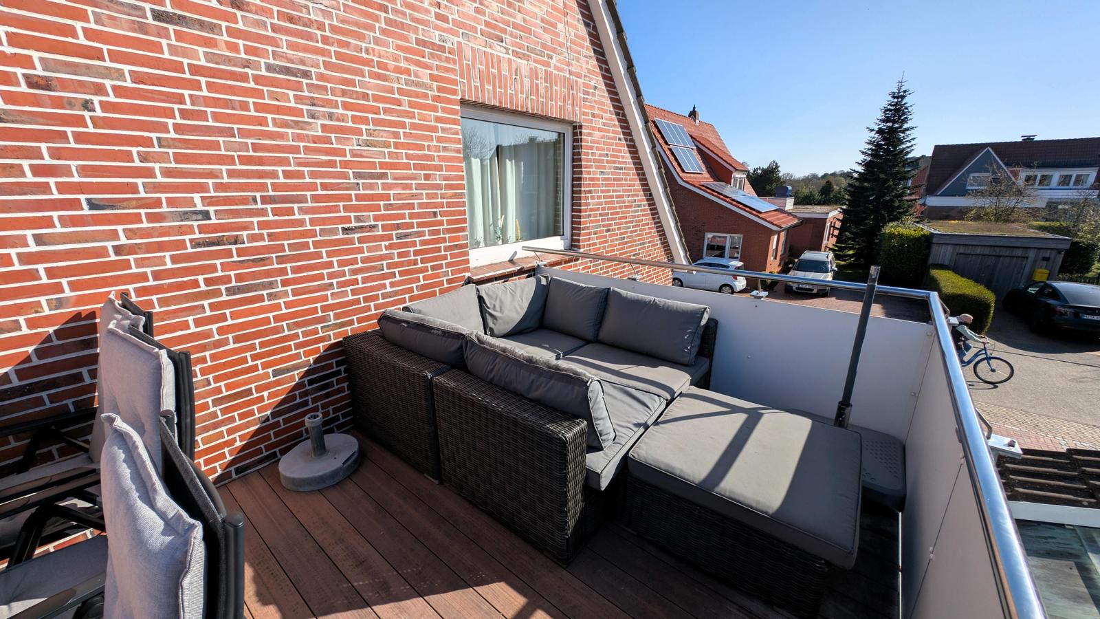 Terrasse mit Sitzgruppe, Holzboden und Blick auf Wohngebiet.