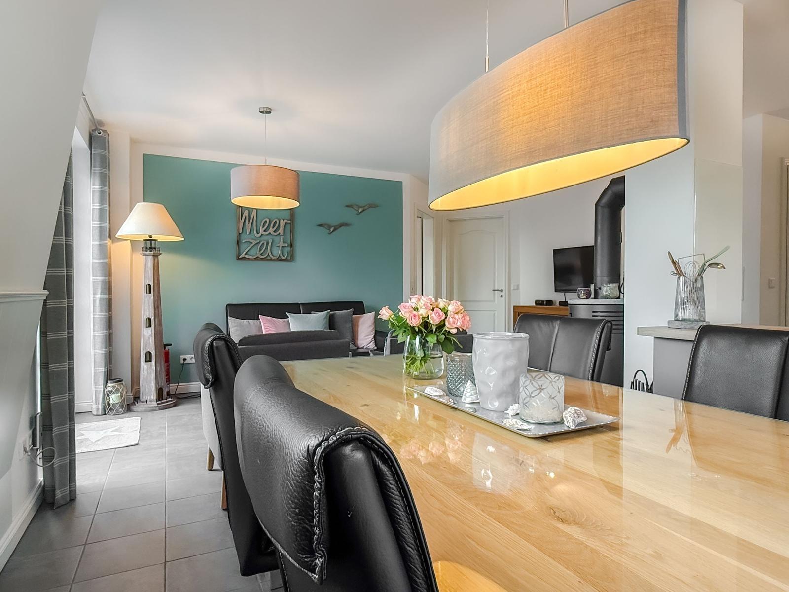 Essbereich mit Holztisch und schwarzen Stühlen. Im Hintergrund Wohnbereich mit Sofa und Wanddekoration.