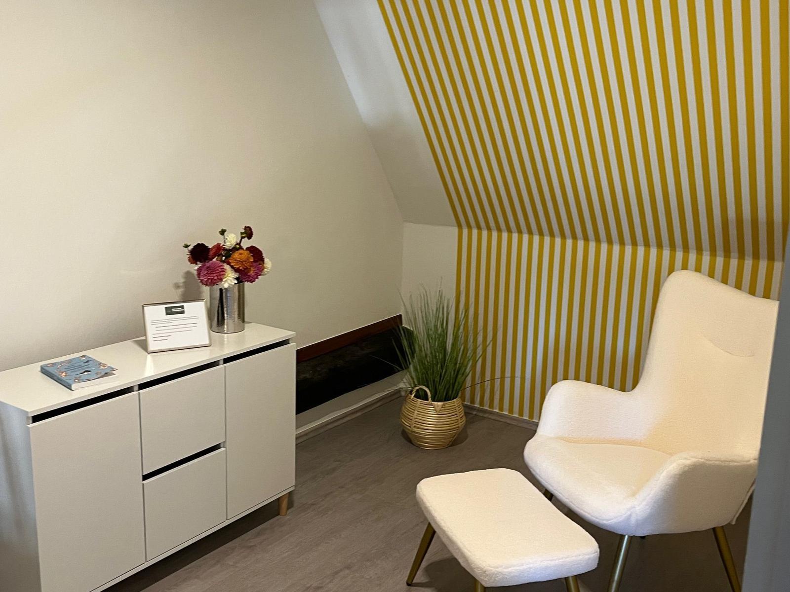 Room with white armchair, cabinet, and striped wall