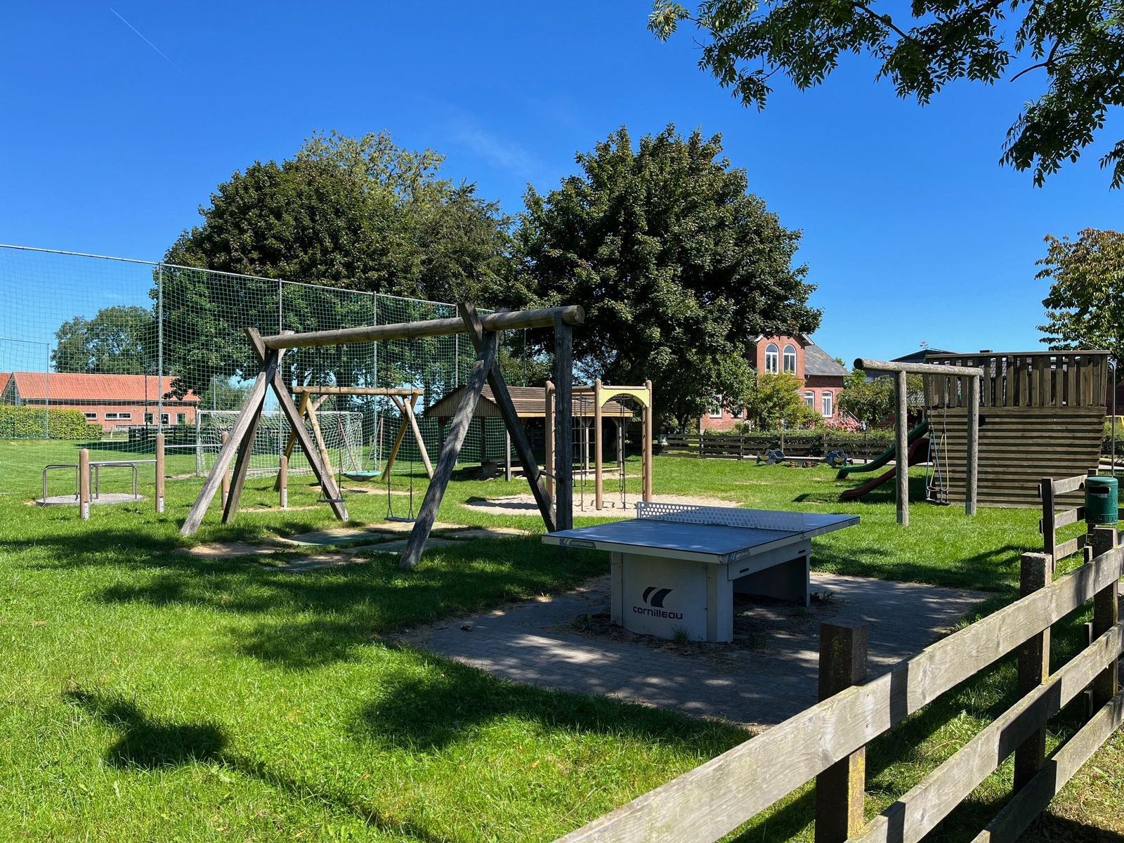 Large playground with swing, slide, and ping pong table on green lawn.