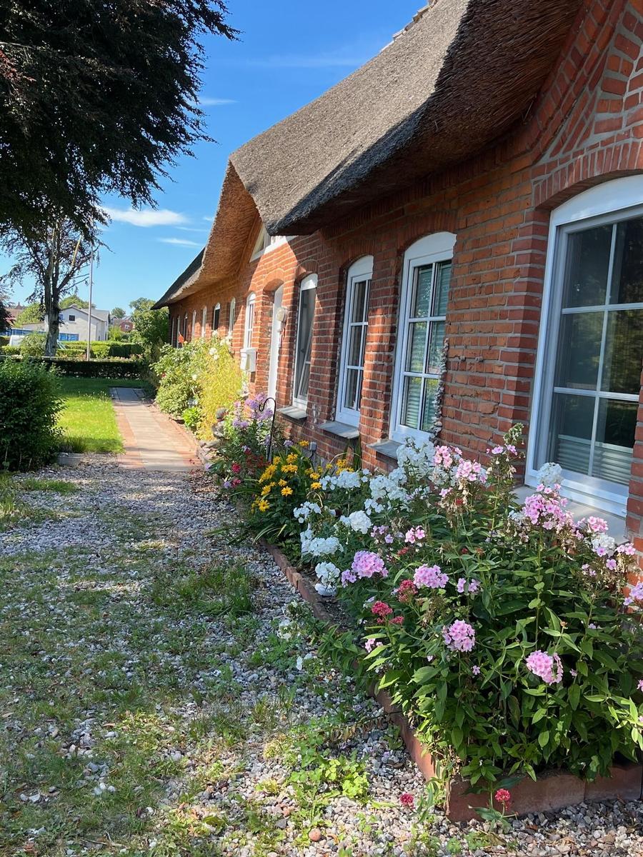 Red brick house with thatched roof and flower beds along a gravel path.