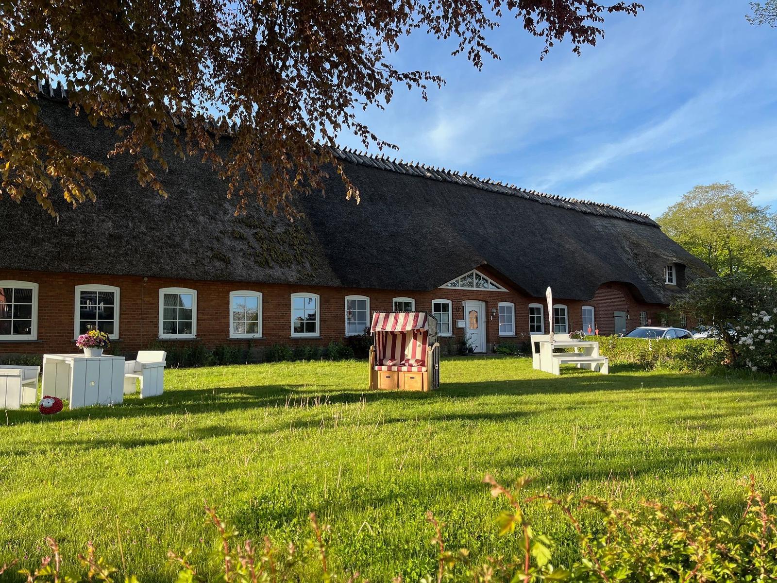 Red brick house with thatched roof and garden with sun lounger.