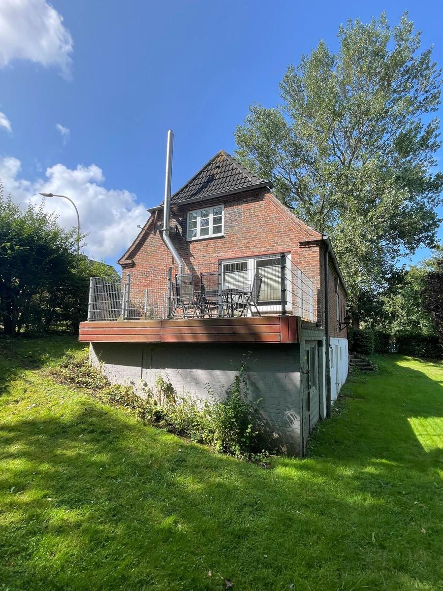 Haus mit Balkon, Grill und Garten. Hoher Dachfirst und roter Ziegelbau.