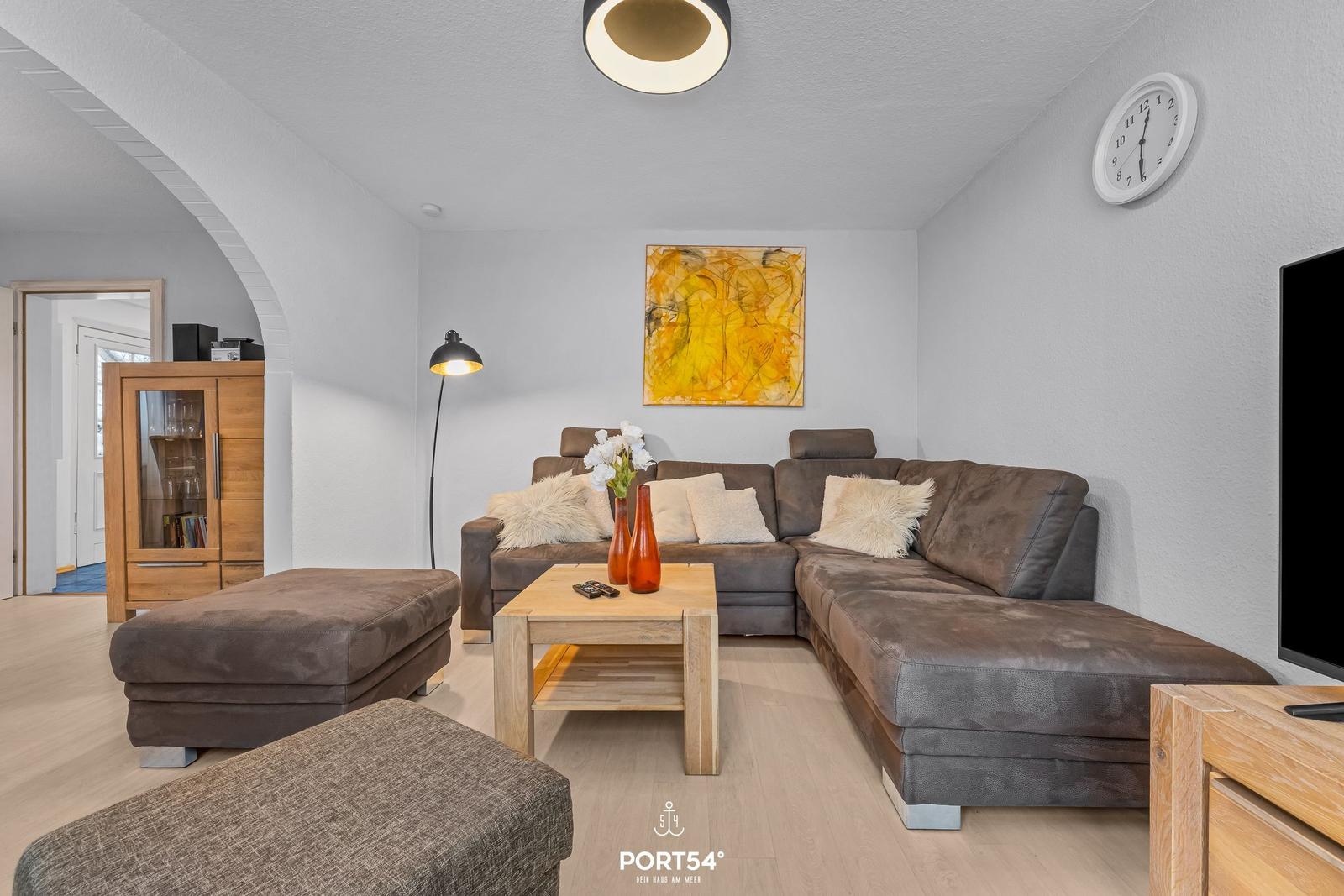 Wohnzimmer mit braunem Sofa, Holztisch und Wanduhr.