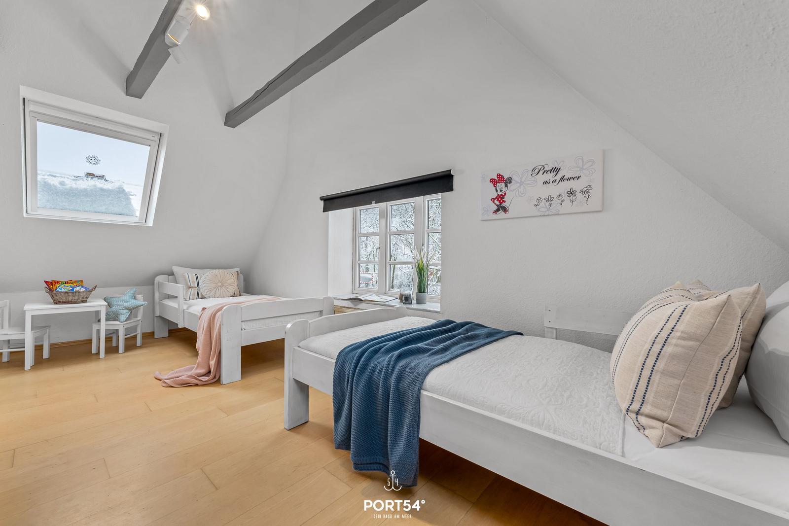 Zwei weiße Betten mit Decken und Kissen. Holzboden, Fenster und Dachschrägen.