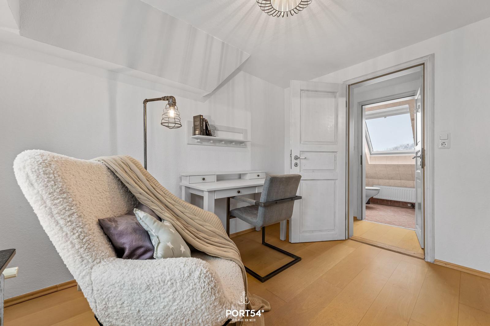 Schlafzimmer mit Schreibtisch, Sessel und Blick in Badezimmer.