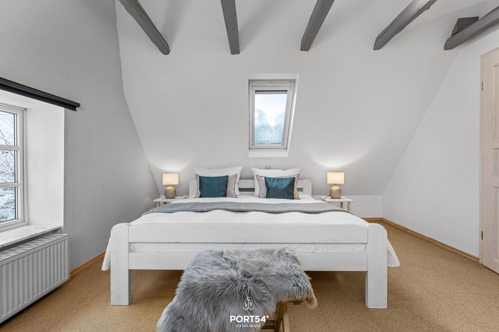 Schlafzimmer mit Dachschrägen, Bett, Nachttischen und Fenstern.
